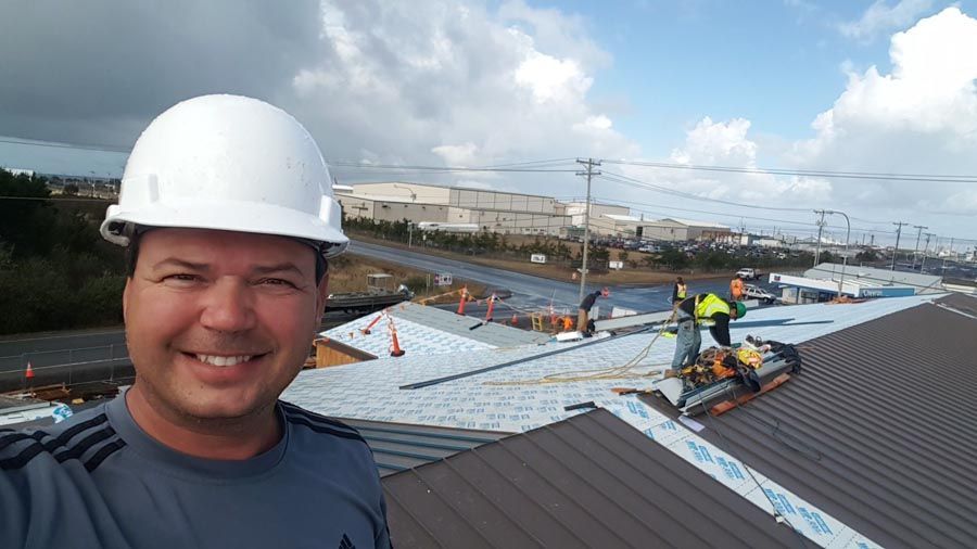 A man wearing a hard hat is standing on top of a roof.