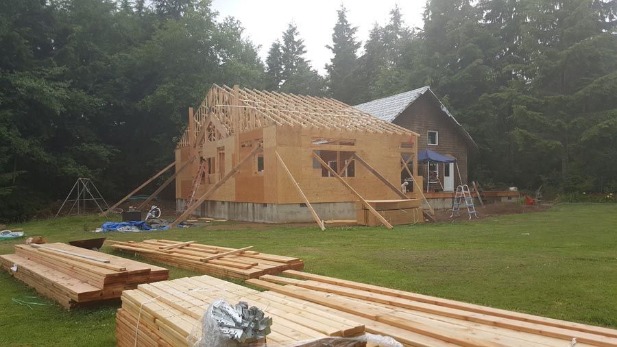A house is being built in a field with a lot of wood in front of it.