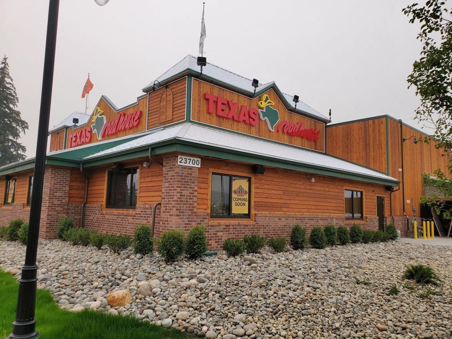 A texas roadhouse restaurant is surrounded by rocks and grass.