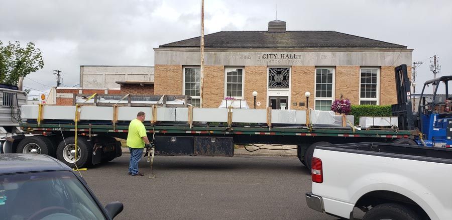 A truck is being loaded with a large piece of metal in front of a building.