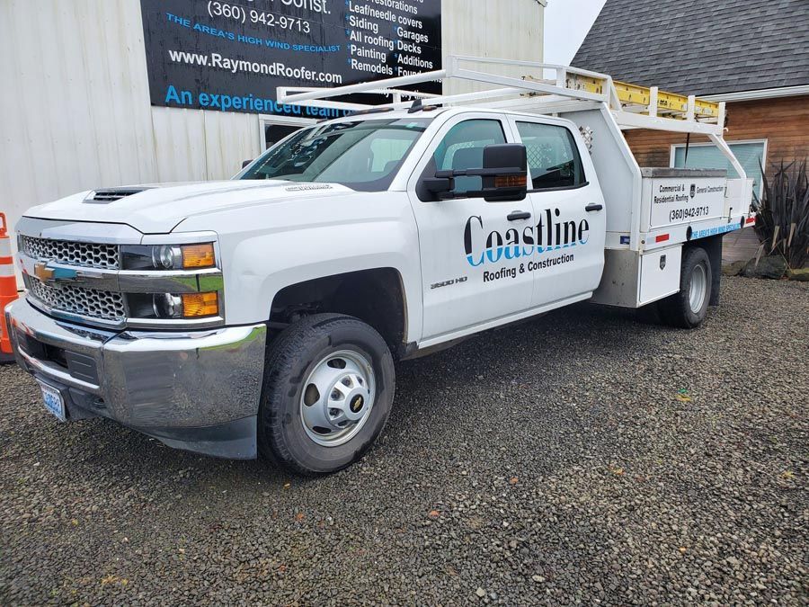 A white truck with the word coastline on the side is parked in a gravel lot.