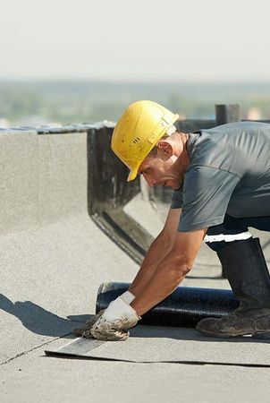 A man wearing a hard hat is working on a roof.