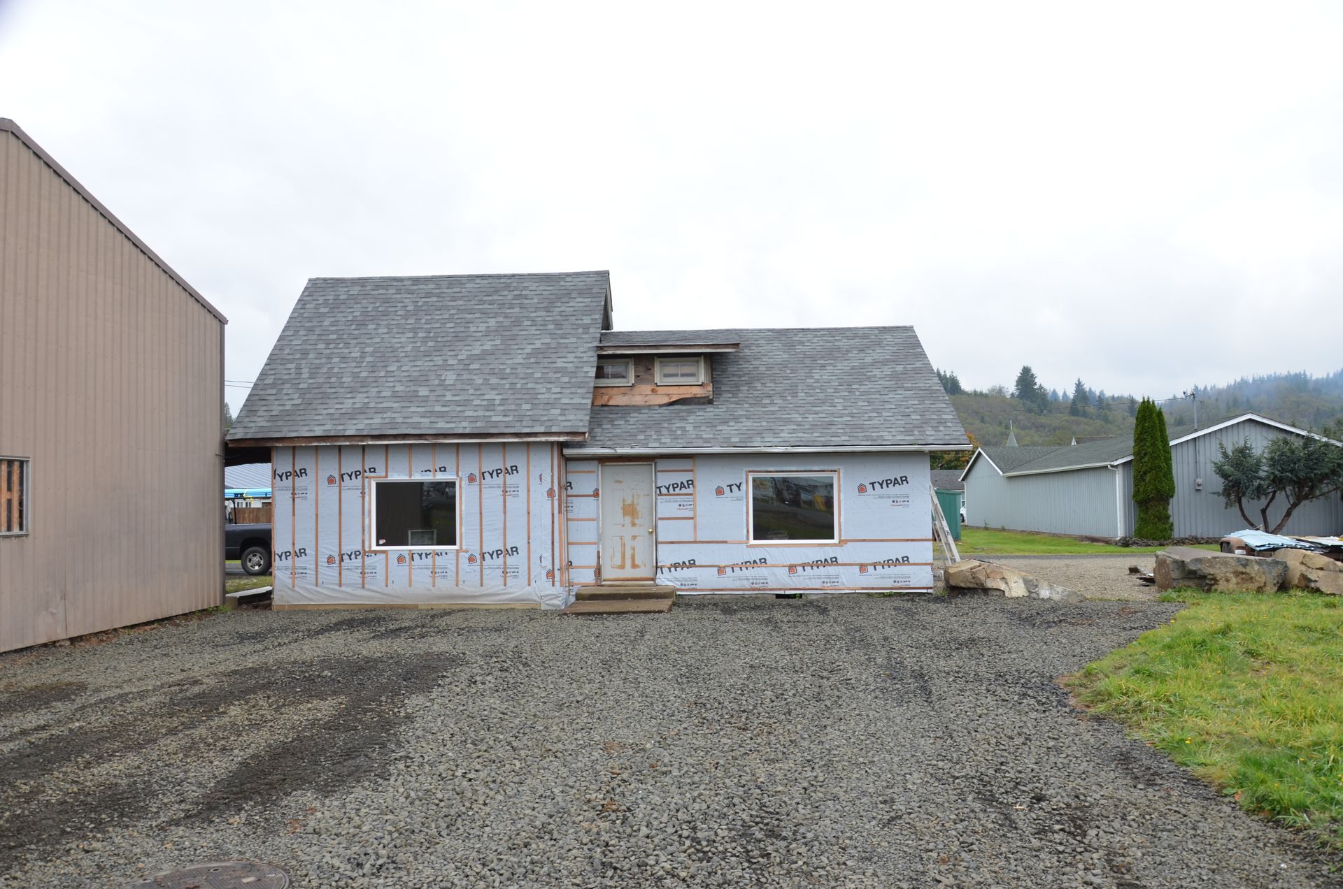 A small house is being built with a gravel driveway in front of it.