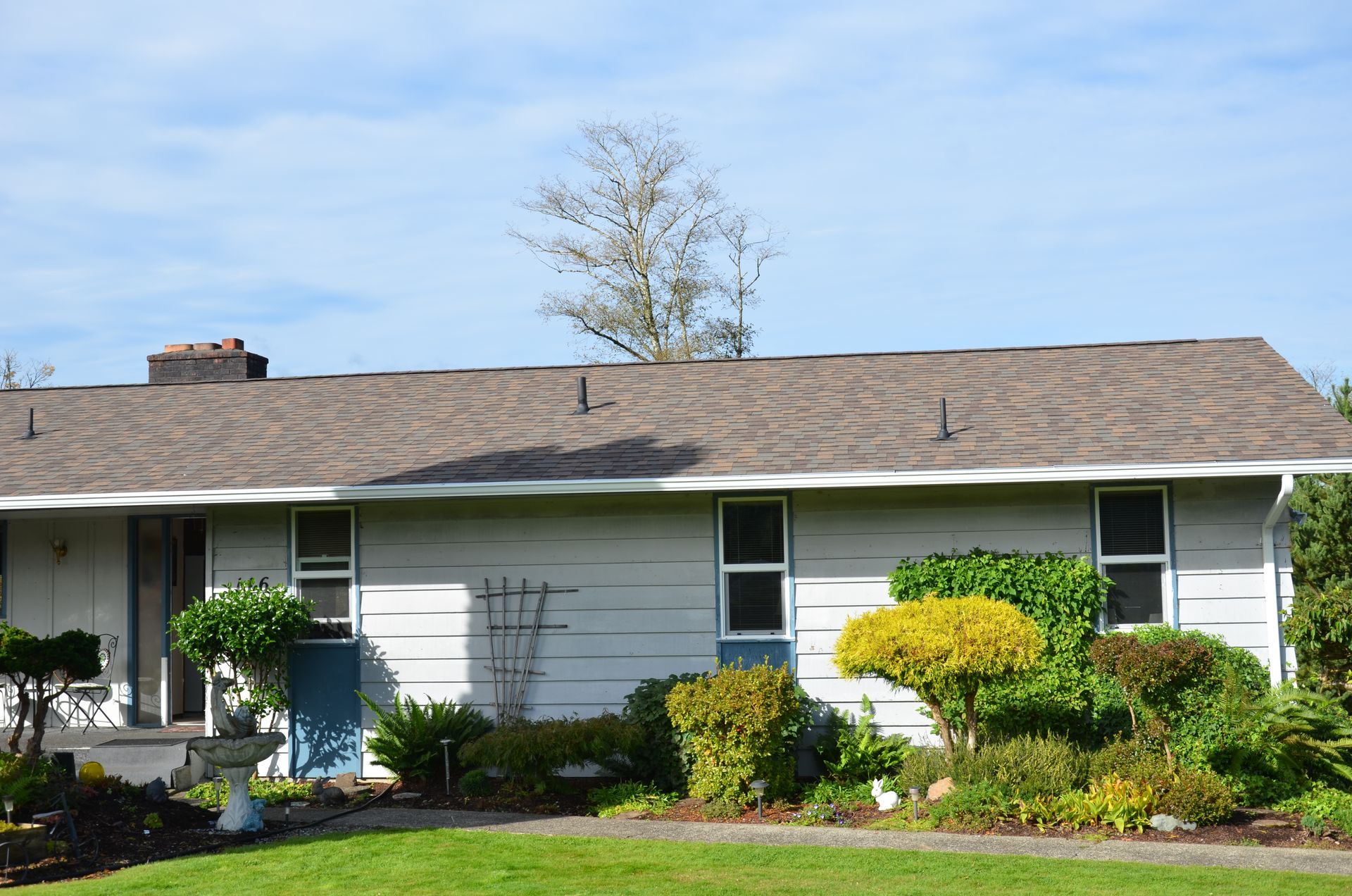 A white house with a brown roof and a lush green yard