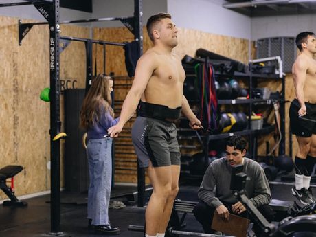 A shirtless man is jumping a jump rope in a gym.