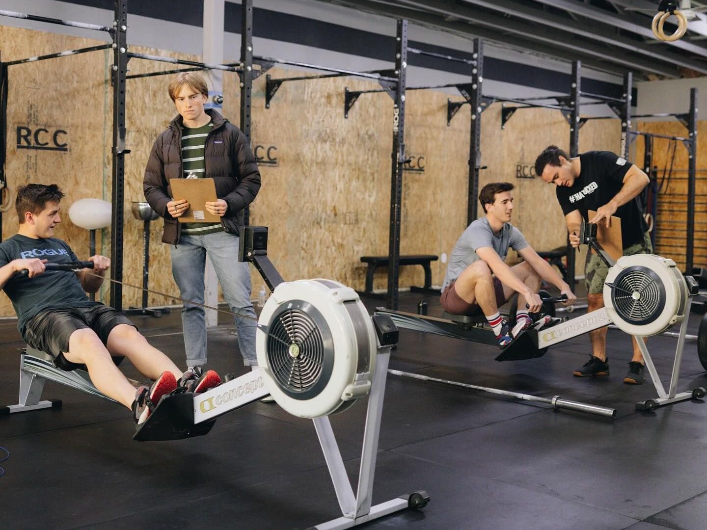 A group of young men are using rowing machines in a gym.