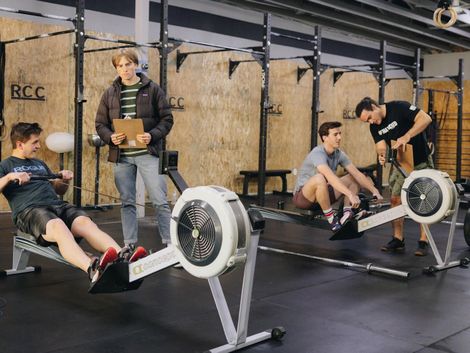 A group of young men are using rowing machines in a gym.