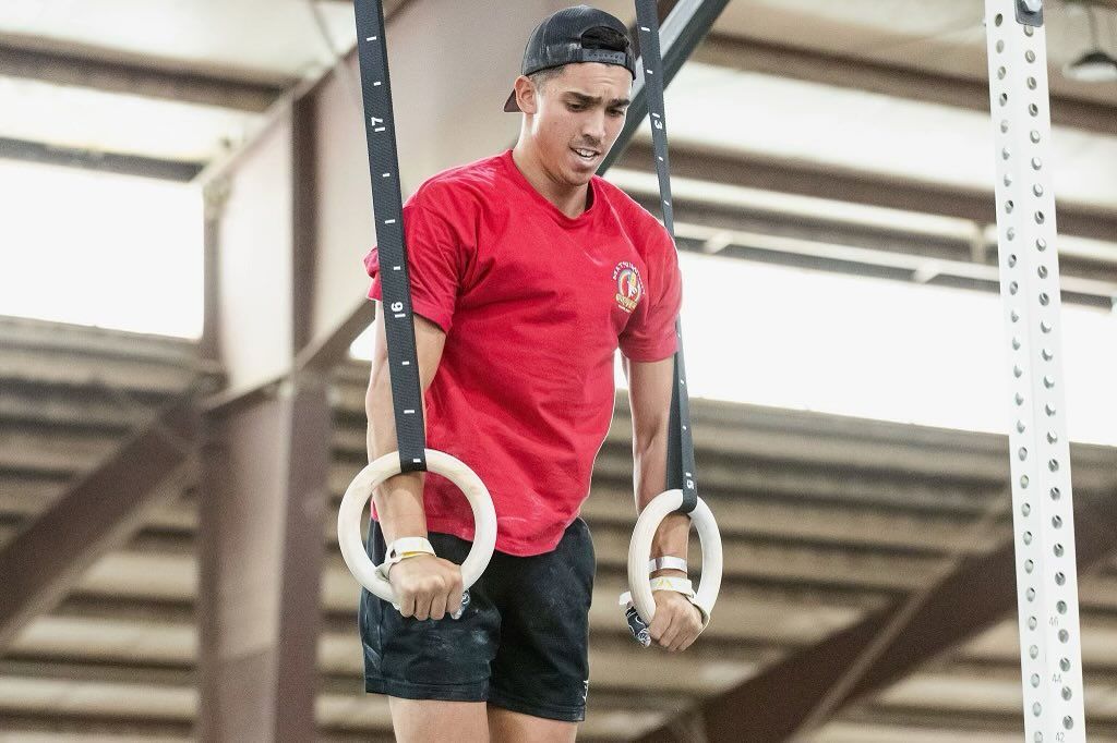 A man in a red shirt is doing exercises on gymnastic rings.