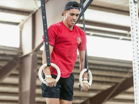 A man in a red shirt is doing exercises on gymnastic rings