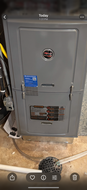 A gray furnace with a circular logo on the front panel and a white pipe connected at the bottom.
