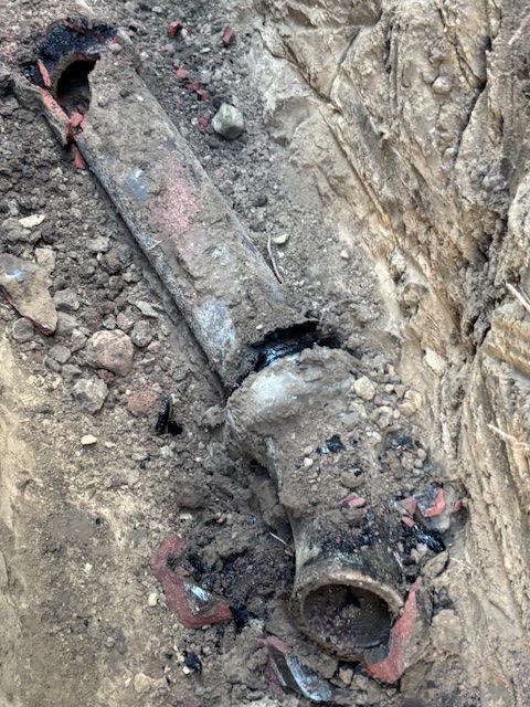 Broken clay sewer pipe in excavated ground.
