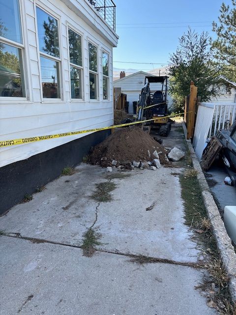 A small excavator next to a building with yellow caution tape, dirt pile on cracked concrete.