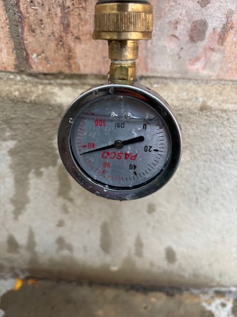 Close-up of a Pasco pressure gauge connected to an outdoor spigot; the gauge reads 0 PSI.
