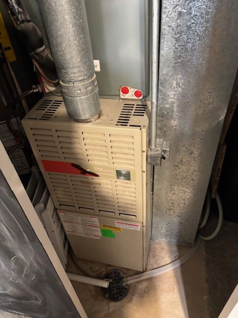 Furnace in a utility room with metal ductwork and a white exterior.
