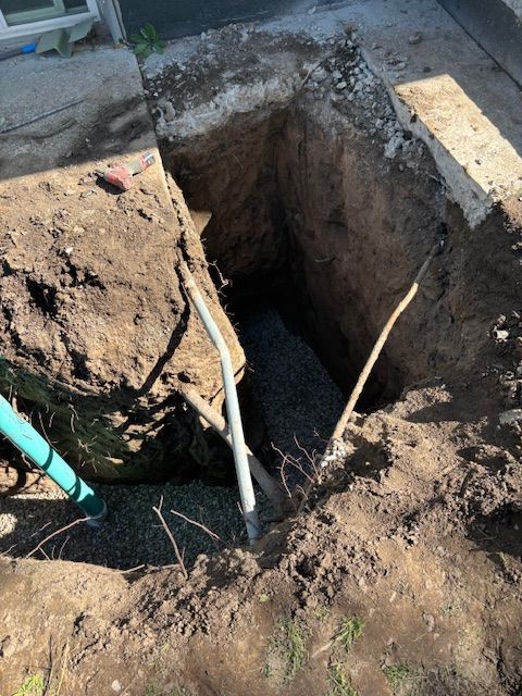 Open rectangular hole dug in ground, with shovel and gravel visible.
