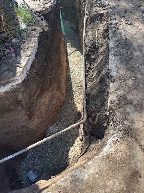 Trench filled with gravel, a pipe running through it, alongside concrete, and dirt.