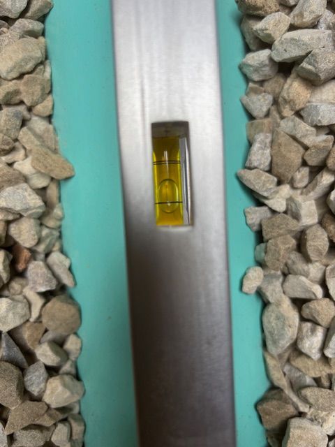 A level tool shows a bubble centered between two lines on a turquoise surface with rocks on either side.