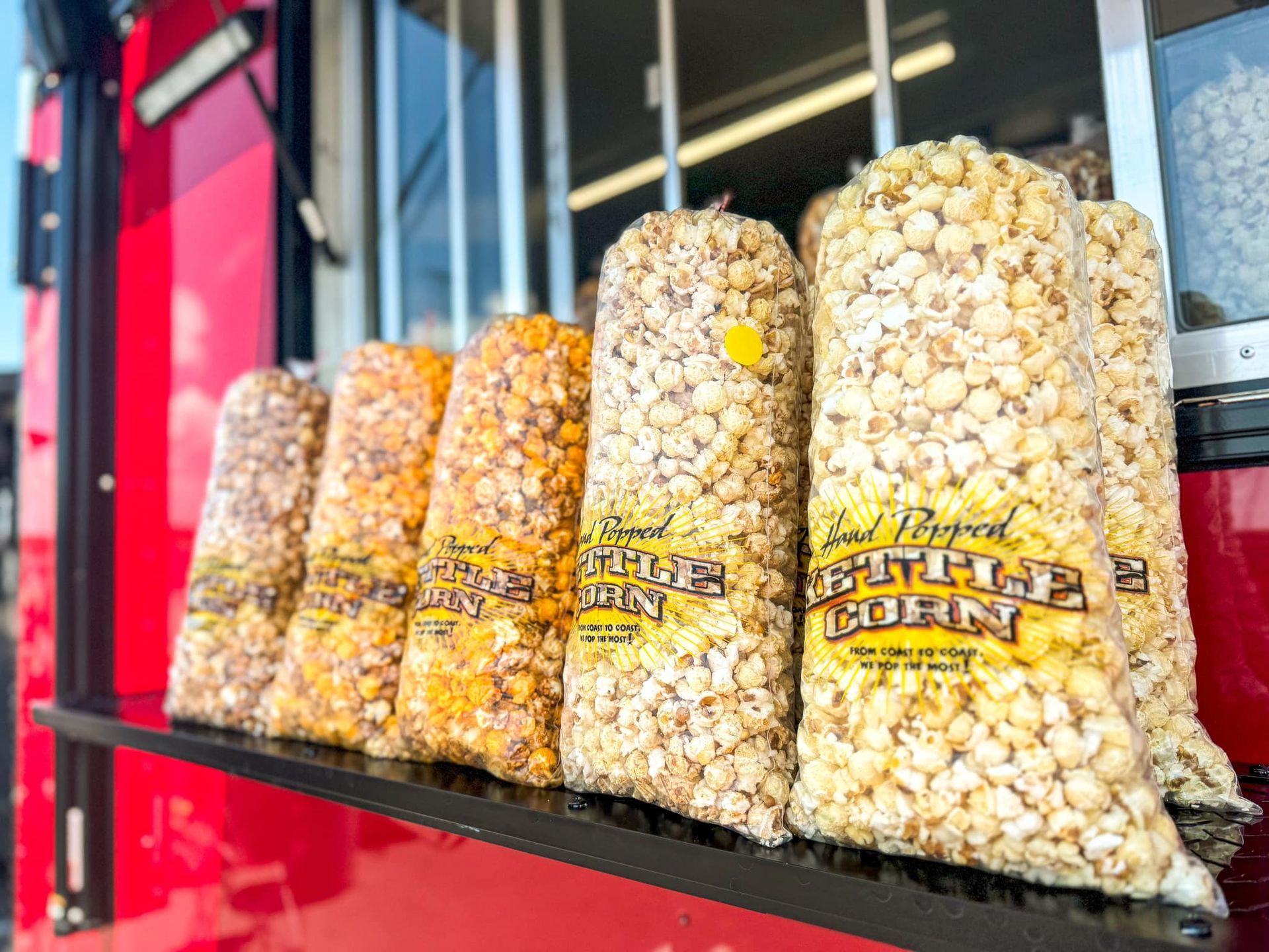 Bags of popcorn are lined up on a shelf in front of a window.