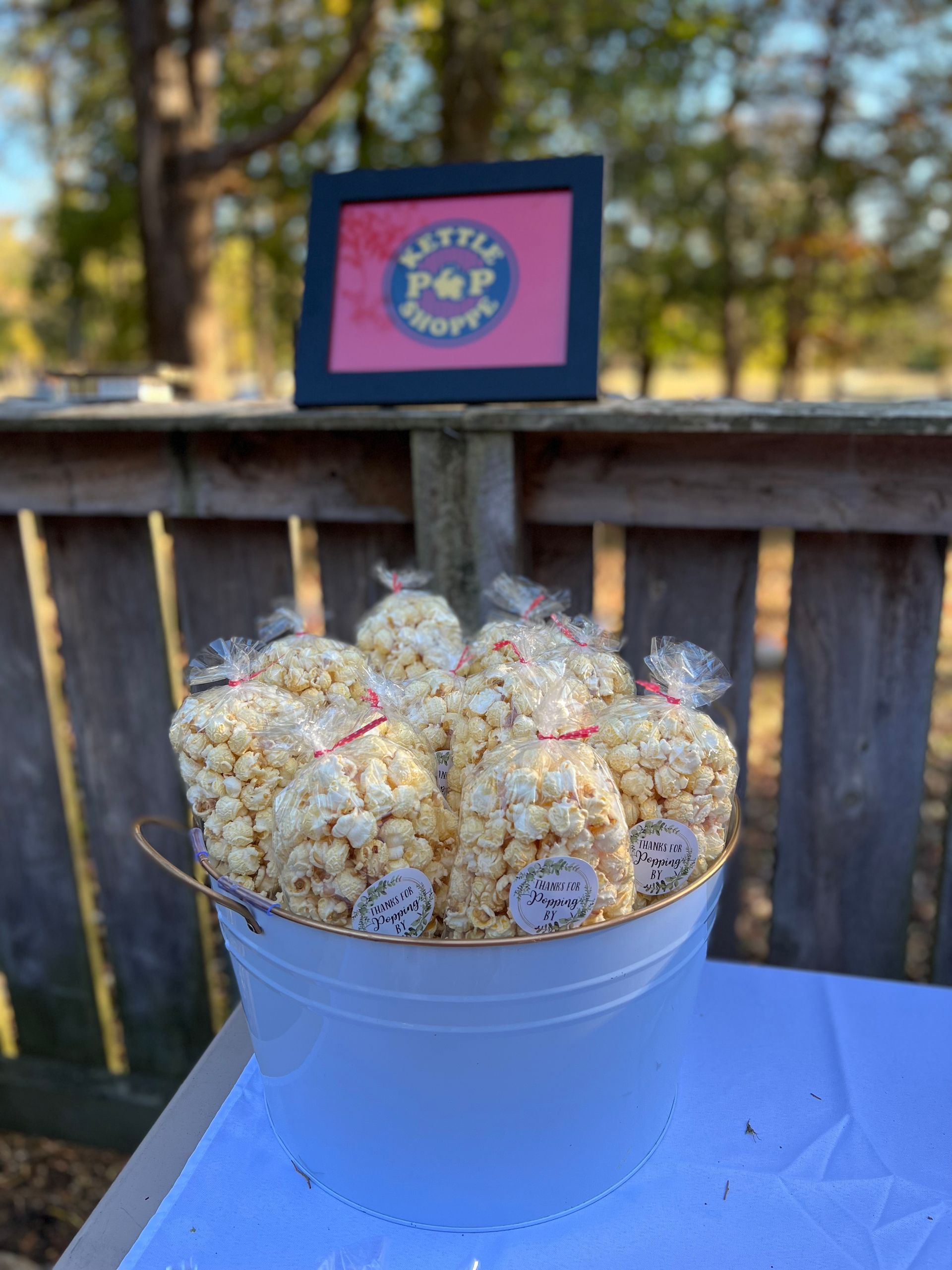 A bucket of popcorn is sitting on a table next to a wooden fence.
