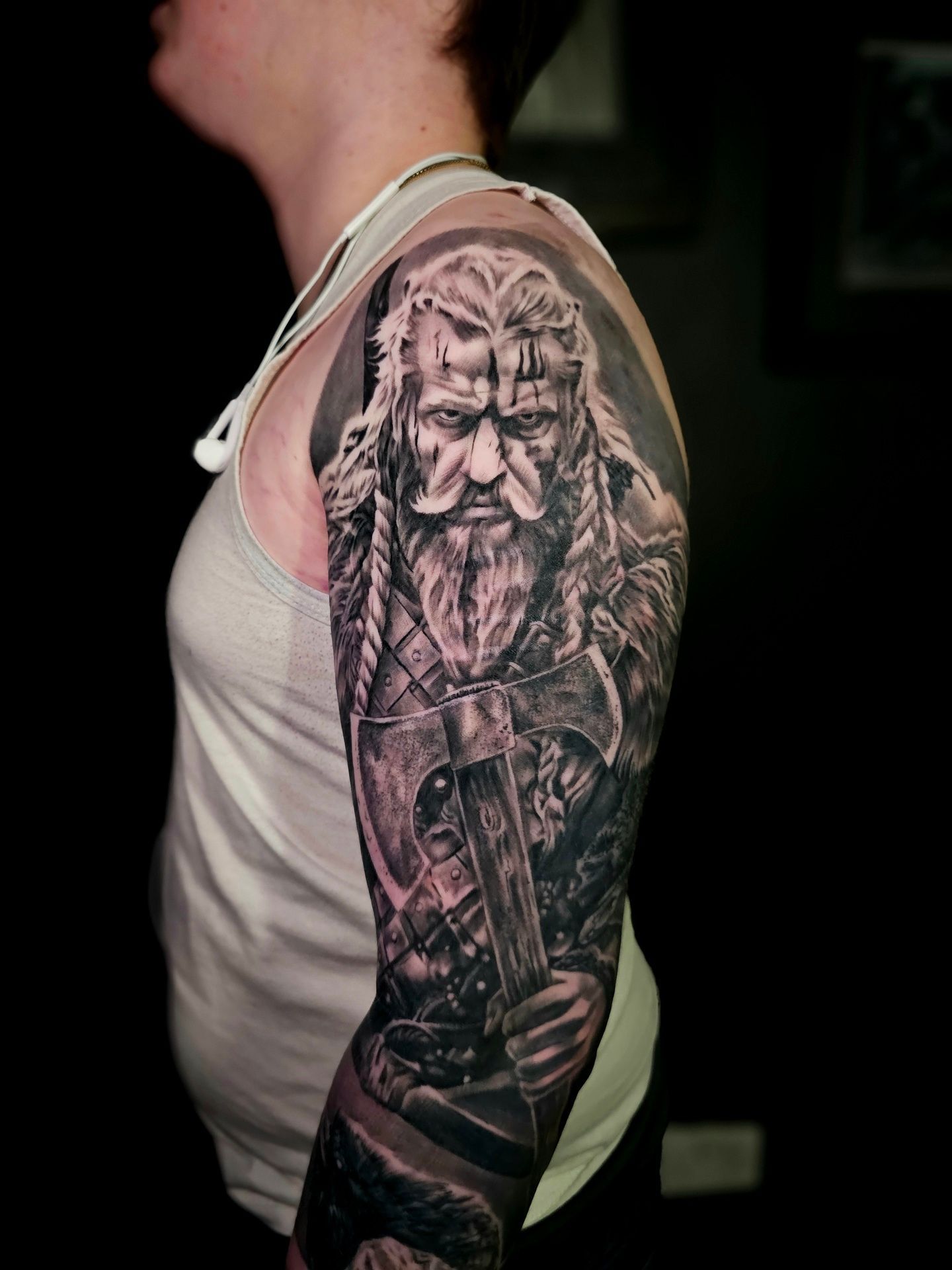 A person with a detailed, black-and-grey tattoo of a bearded warrior on their upper arm, holding an axe.