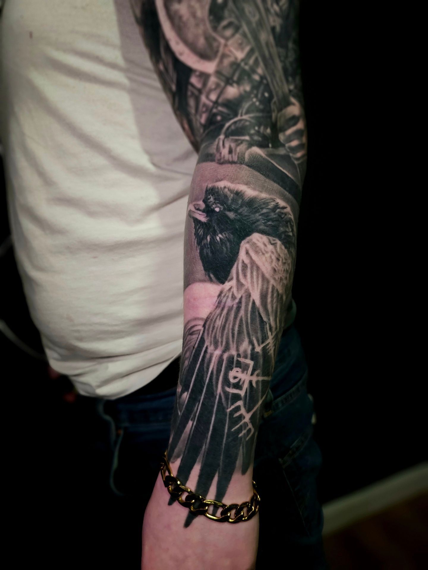 A close-up of a person's forearm featuring a detailed black and grey tattoo of a bird and Nordic symbols.