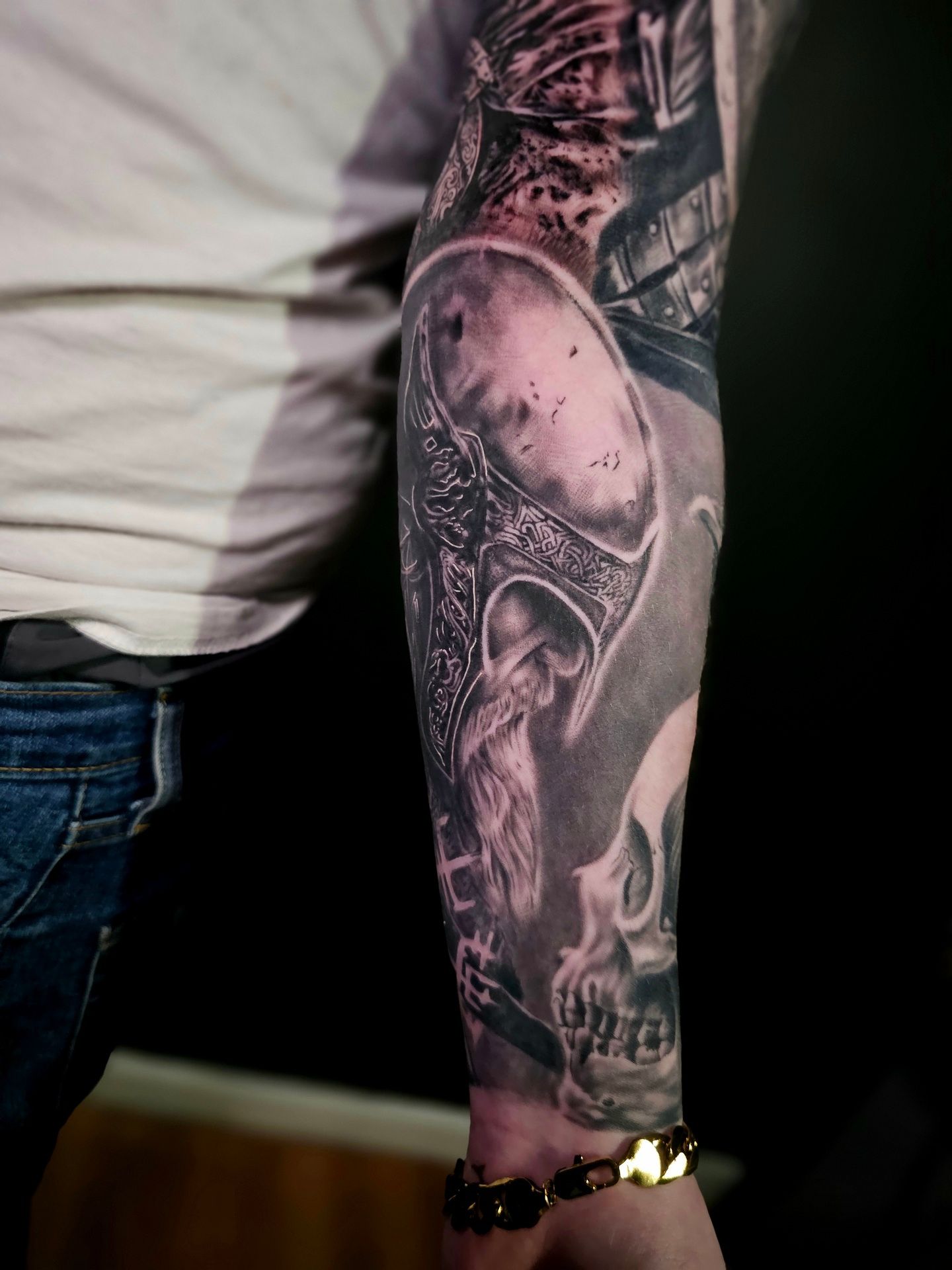 A black and grey forearm tattoo featuring a Viking warrior in a helmet, a skull, and intricate, dark shading.