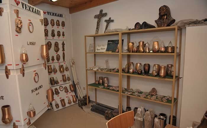 Scaffali espositivi in uno showroom con varie urne funerarie in bronzo, targhe commemorative e croci religiose.