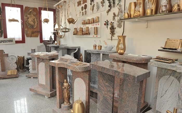 Interno di un negozio con vari piedistalli in pietra, lapidi, vasi in bronzo e oggetti decorativi religiosi.