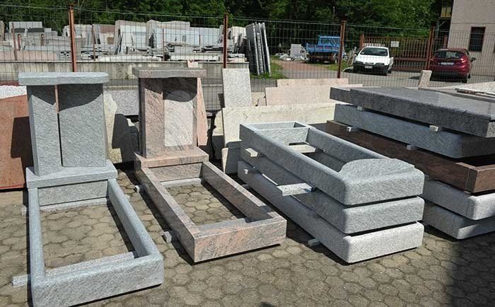 Diverse lapidi e cornici tombali in pietra sono esposte all'aperto in un laboratorio o in un'area di vendita.