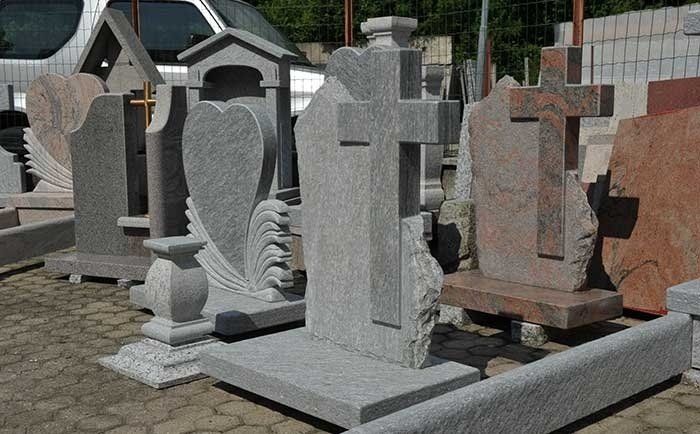 Una selezione di lapidi e monumenti in pietra di diverse tonalità, grigie e rossastre, esposti su un piazzale pavimentato.