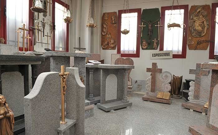 Lo showroom di uno scalpellino che espone diverse lapidi in granito, croci e sculture murali a tema religioso.