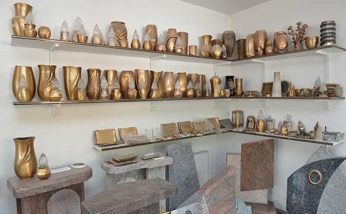 Una sala espositiva con scaffali pieni di varie urne dorate, vasi e monumenti commemorativi in pietra.
