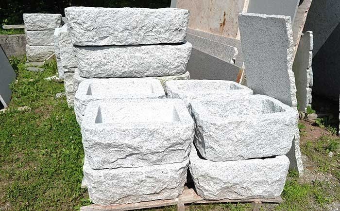 Una pila di fioriere in granito grezzo grigio chiaro, appoggiate su un pallet di legno all'aperto su una superficie erbosa.