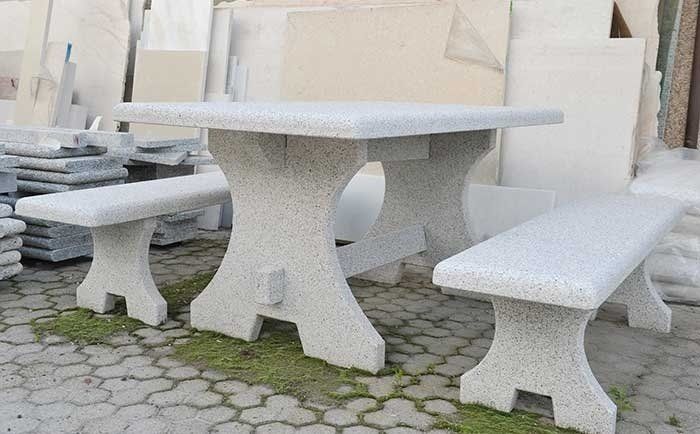 Un set da patio in cemento grigio chiaro con effetto maculato, composto da un tavolo rettangolare con base a forma di X e due panchine abbinate.