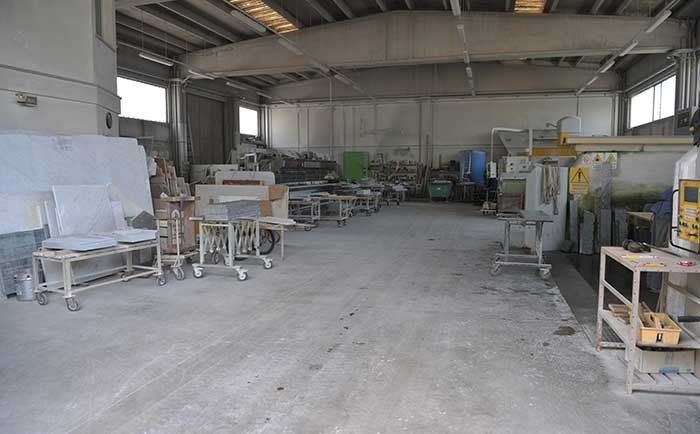 Interno di un magazzino con macchinari industriali per il taglio della pietra, tavoli da lavoro e pile di lastre di pietra.