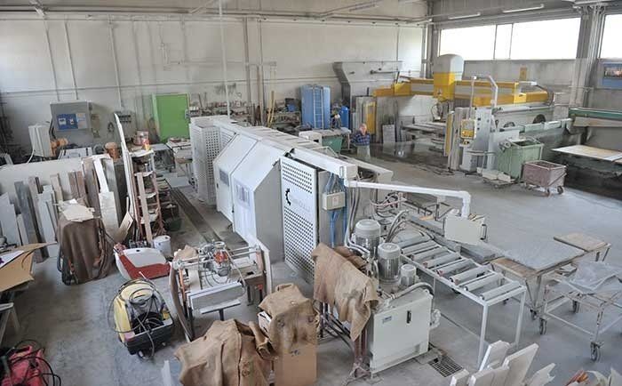 Un'officina industriale è caratterizzata da grandi macchinari per il taglio della pietra, nastri trasportatori e lastre di pietra disposte in un'area di lavoro.