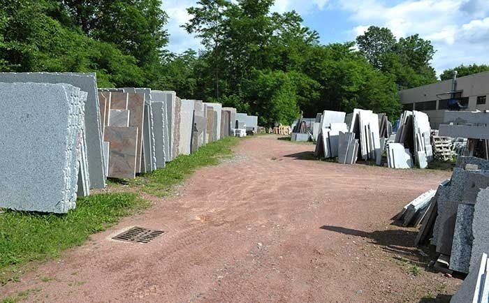 Grandi lastre di pietra, disposte all'aperto in file su entrambi i lati di un sentiero di terra rossastra che conduce verso gli alberi.