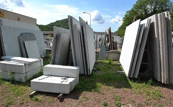 Grandi lastre di pietra stoccate all'aperto in un cortile, con pile di blocchi finiti a terra.