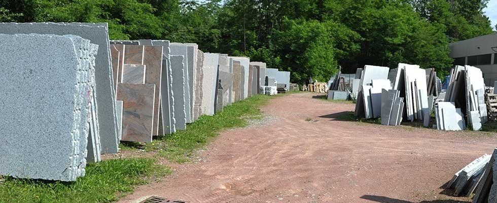 In un piazzale ghiaioso delimitato da alberi, file di grandi lastre di pietra verticali di vari colori e consistenze si ergono all'aperto.