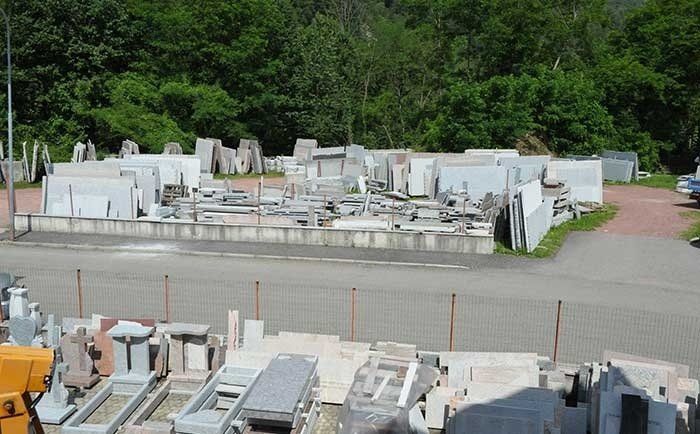 Un cortile in pietra, all'aperto vicino a una foresta, con varie lastre di marmo e granito, monumenti e lapidi.