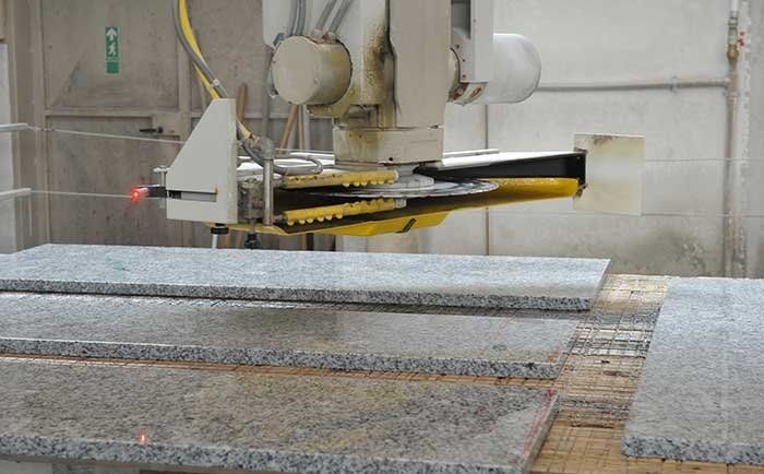 Un braccio robotico con una lama circolare taglia lastre di pietra in un'officina.