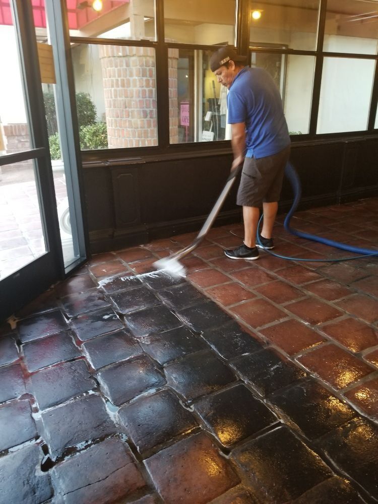 A man is cleaning a brick floor with a vacuum cleaner.