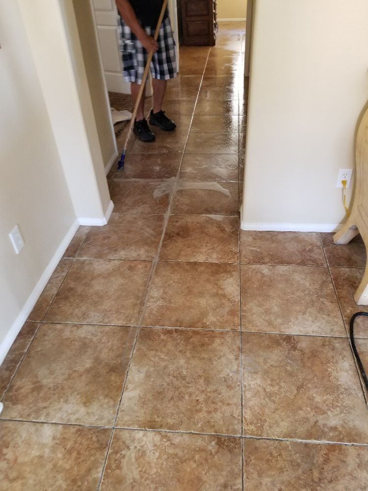 A man is cleaning a tiled floor with a broom.