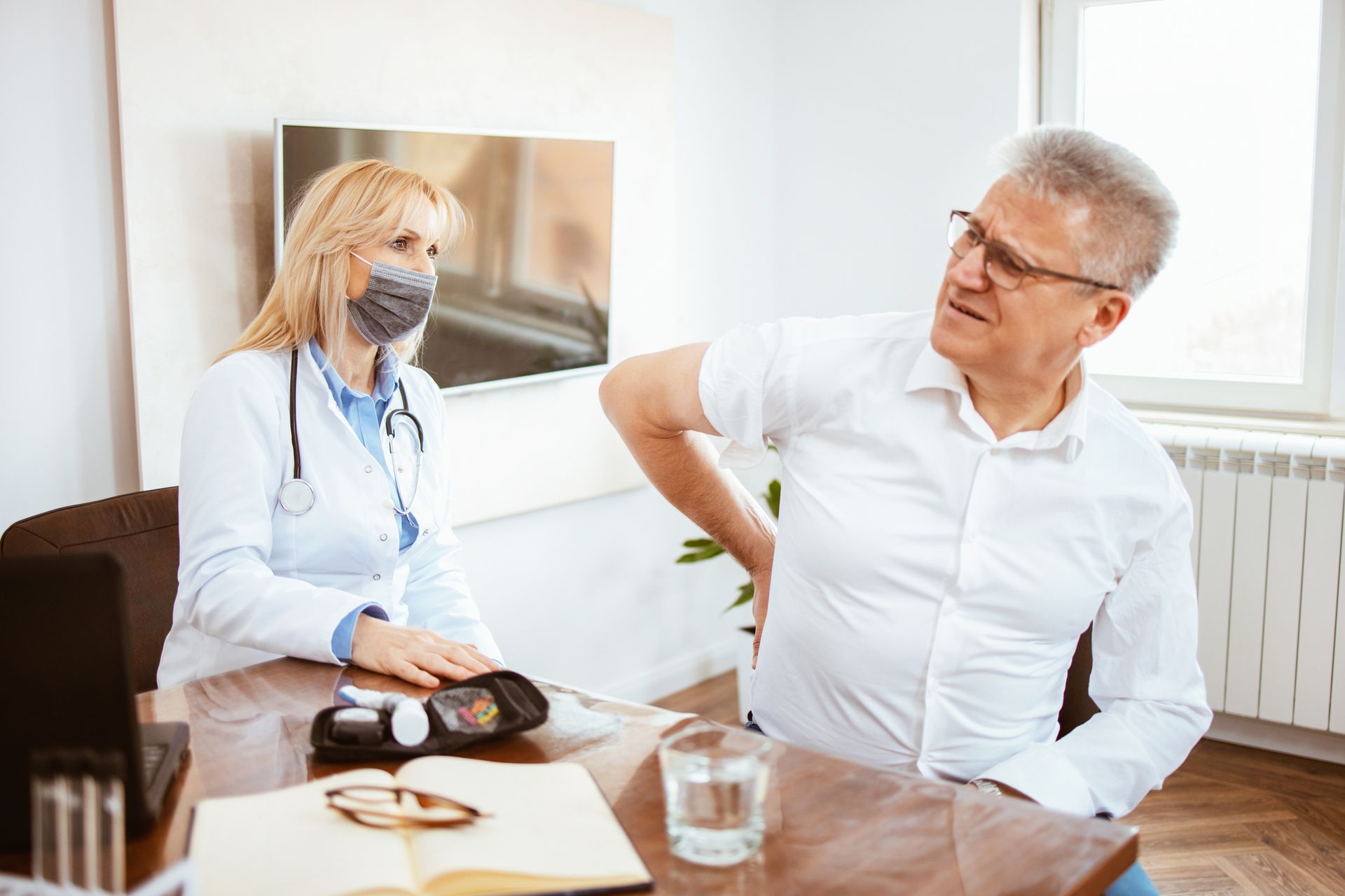 A man is sitting at a table talking to a doctor who is wearing a mask.