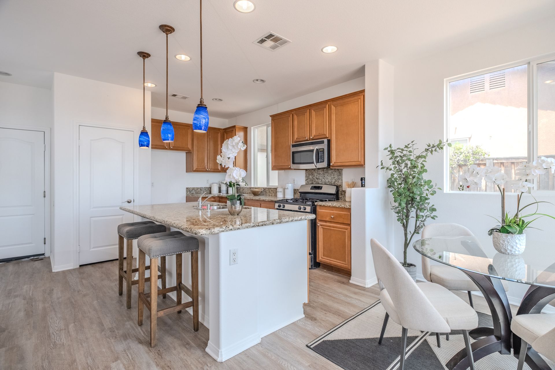 Bright kitchen with island seating, pendant lights, and breakfast nook with glass table.