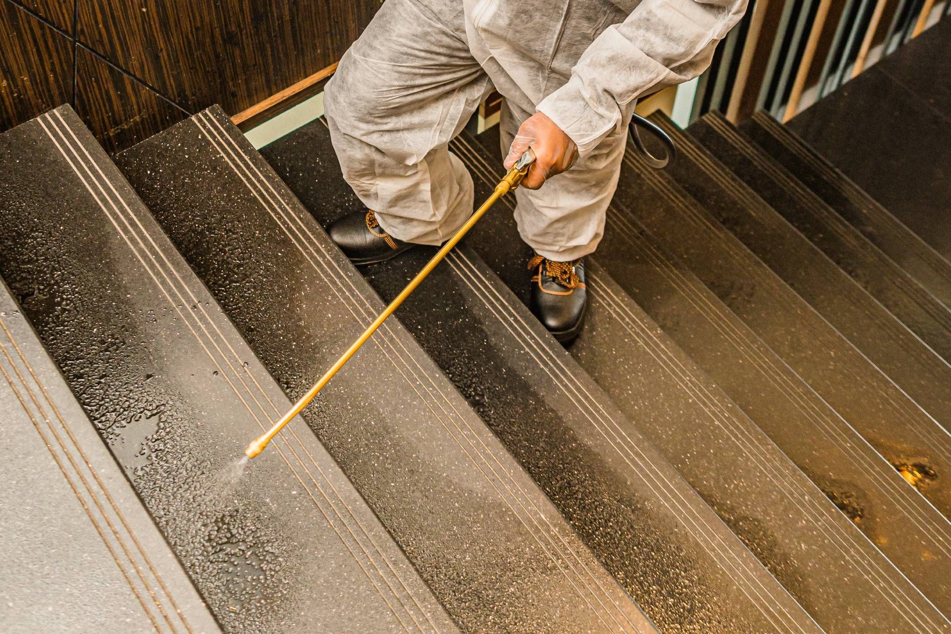 Person in protective suit spraying disinfectant on stairs.