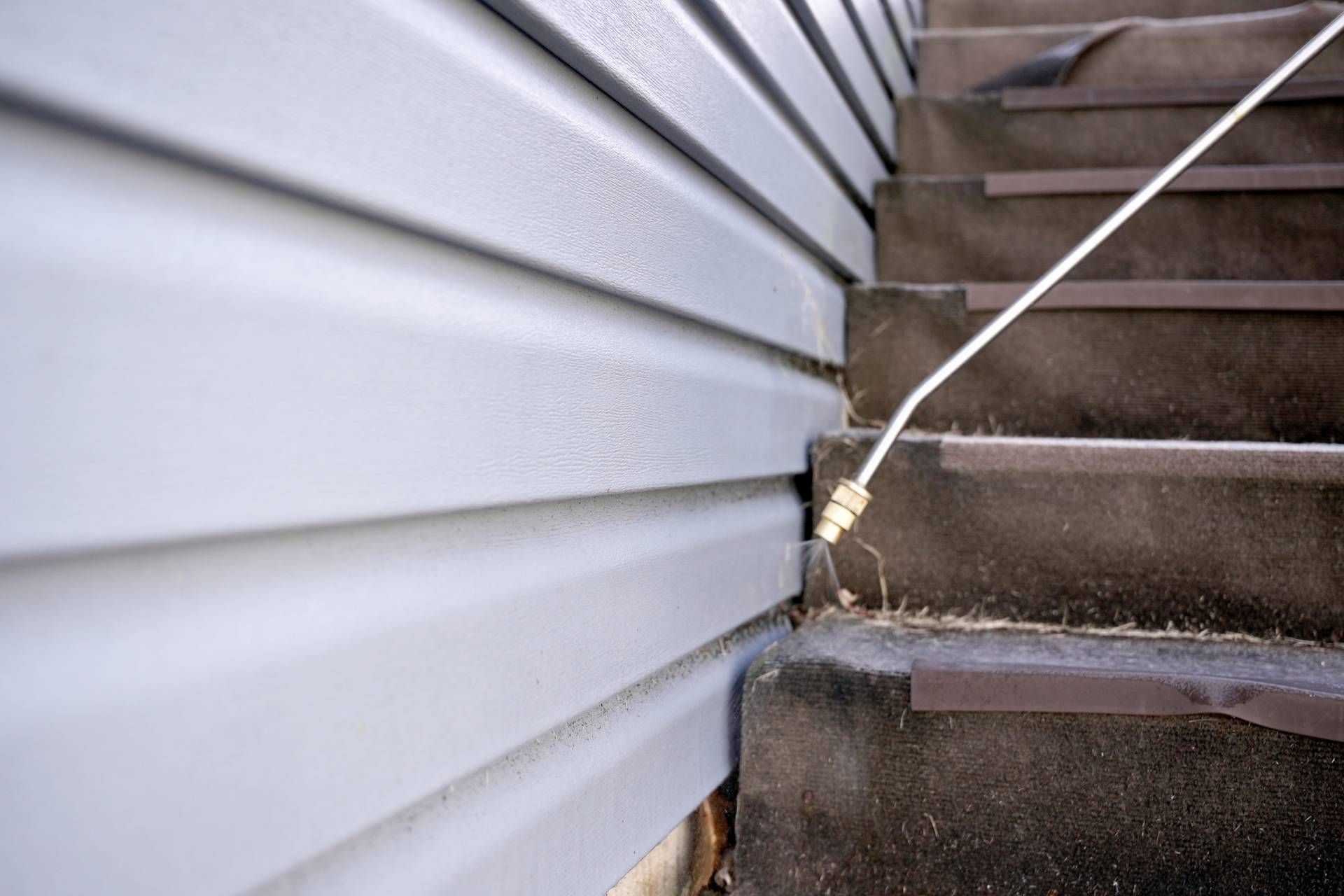 Gray siding and concrete stairs, a thin white hose spraying.