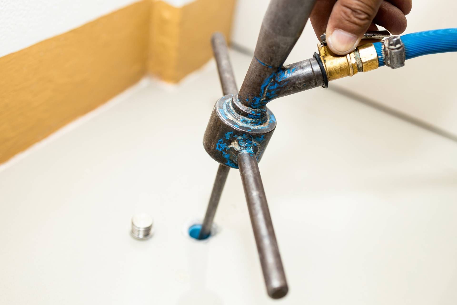 Person using a water test tool in a white-tiled space, examining a drilled hole. A blue hose and brass valve are connected.
