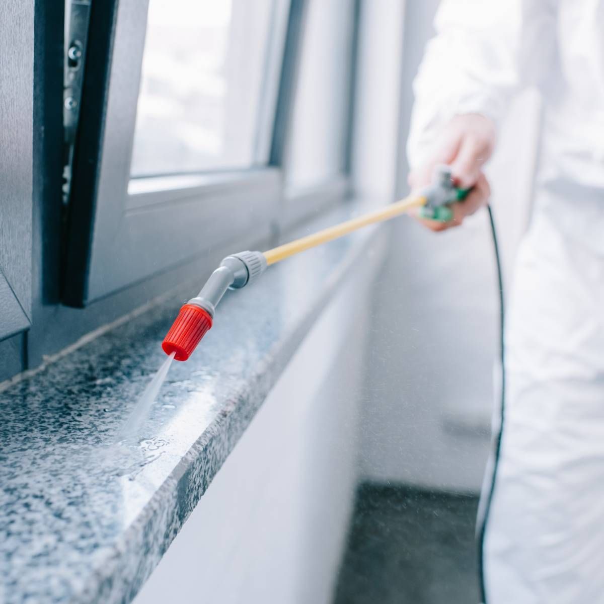 Person in protective suit spraying insecticide on a windowsill.