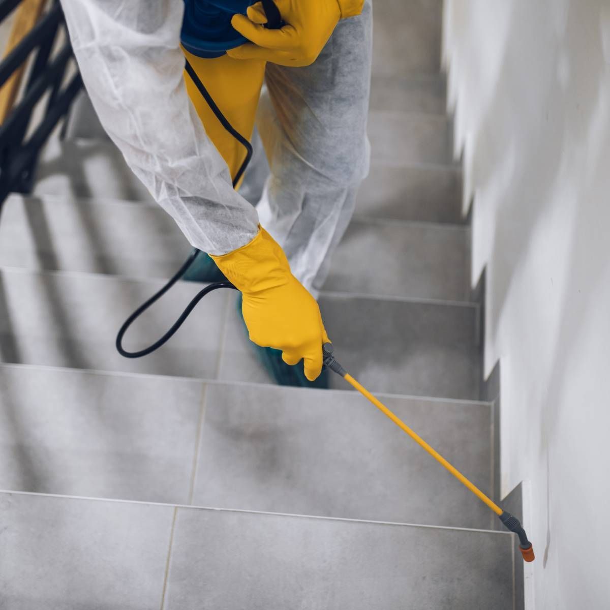 Person in protective suit spraying insecticide on stairs.